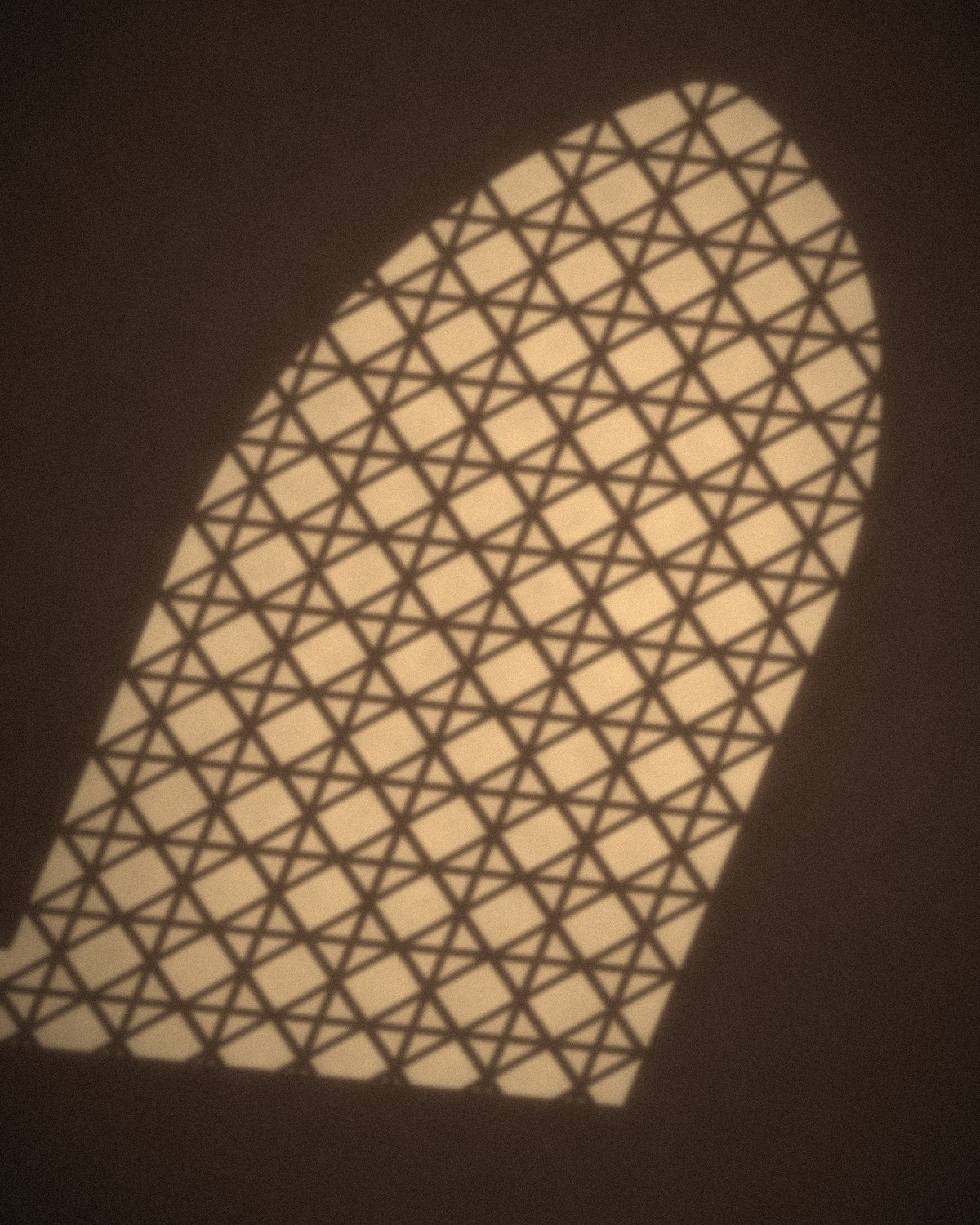 Afternoon light falling through a carved jaali screen onto a sandstone wall